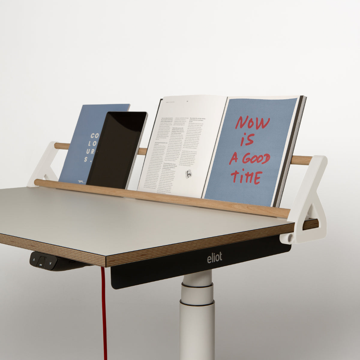 Auf einem Schreibtisch mit einer weißen Holzleiste liegen eine blaue Broschüre, ein schwarzes Tablet und ein aufgeschlagenes Buch, auf dem in roter Schrift „NOW IS A GOOD TIME“ zu lesen ist. Auf der Vorderseite ist das Logo der Smartfurniture GmbH zu sehen, das auf die clevere Schreibtischorganisation hinweist, die vom innovativen Design des „Tiny Top Schreibtischaufsatz White“ inspiriert ist.