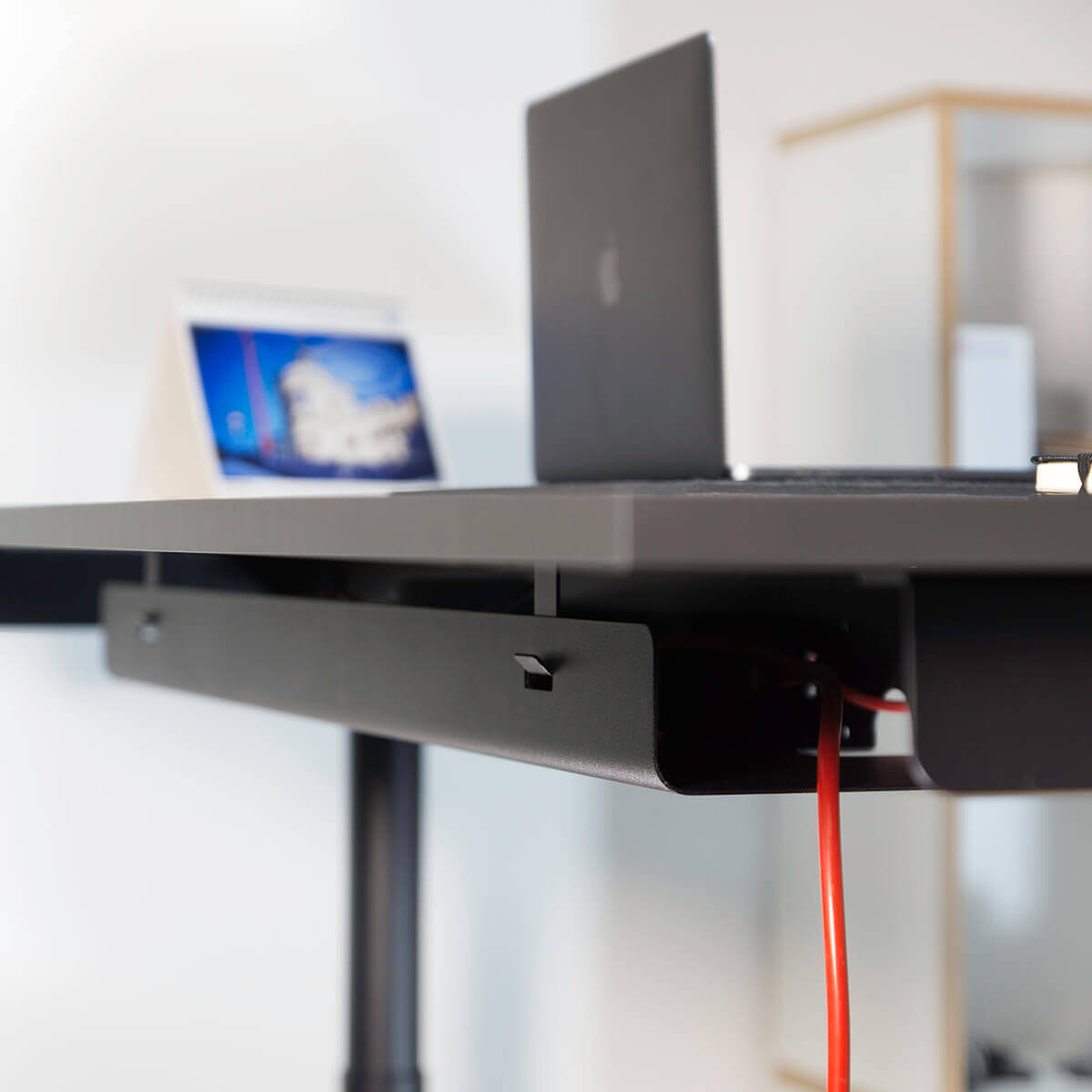 schwarzer Kabelkanal an einem schwarzen Eliot aus dem ein rotes Kabel heraus schaut in einem Bürosetting