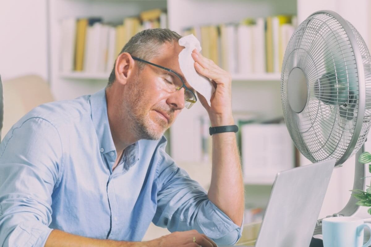 Mann schwitzt wegen Hitze im Büro