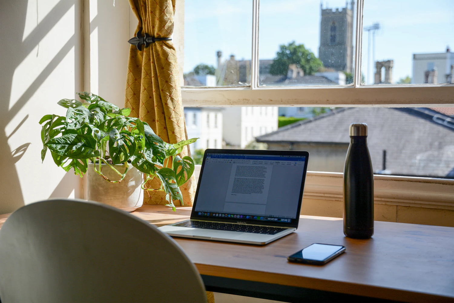 Schreibtisch Homeoffice mit Blick aus dem Fenster und Bierflasche neben Laptop