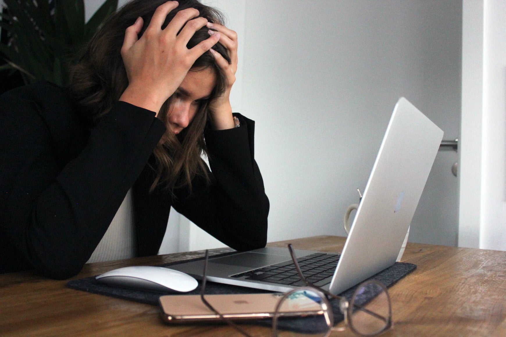 Frau sitzt vor einem Laptop und hält sich vor Stress den Kopf