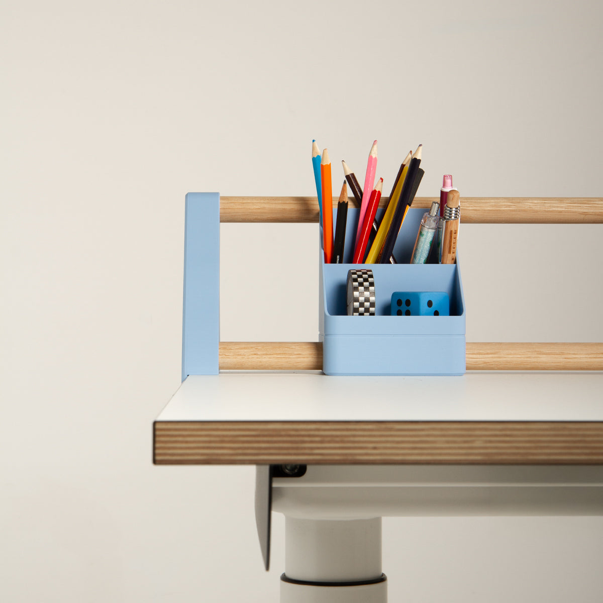 Das „Tiny Top Kids Set Schreibtischaufsatz Hellblau“ von Smartfurniture GmbH bietet Platz für Bleistifte, Kugelschreiber, ein Lineal, Klebeband und Würfel und steht auf der Kante eines Kinderschreibtisches aus hellem Holz und in Weiß, der sich durch ein minimalistisches Design auszeichnet.